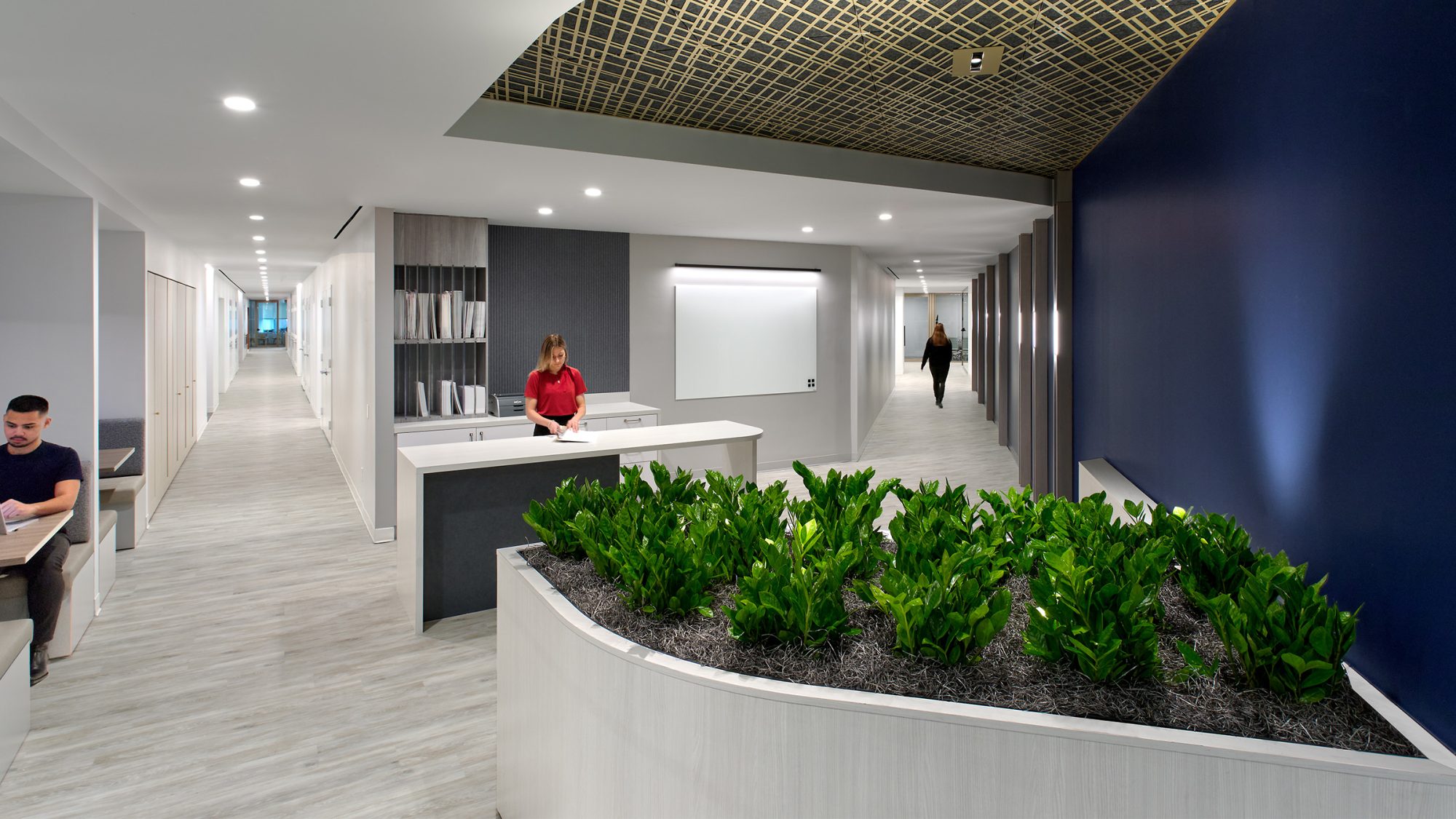 man working in booth, woman at counter and woman walking down corridor